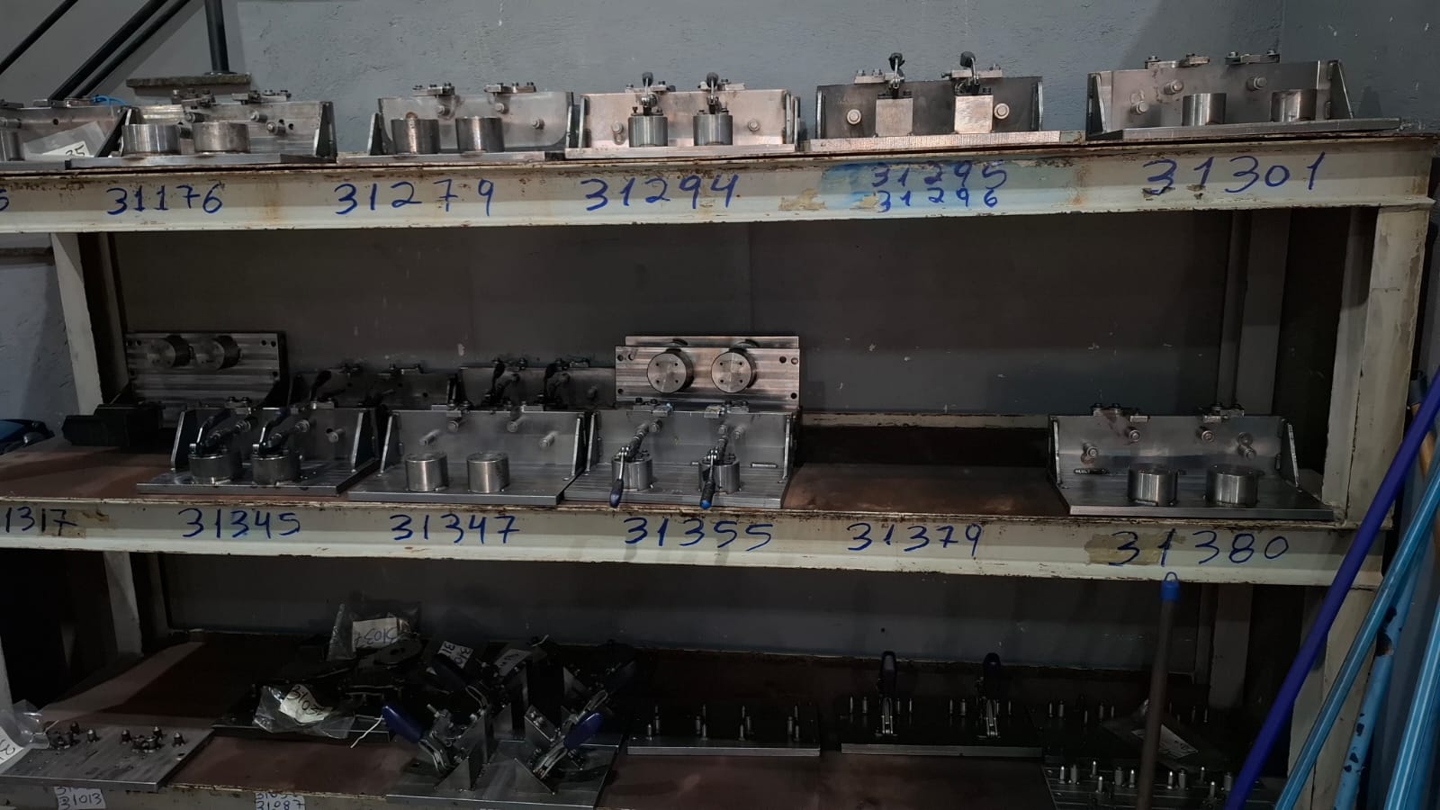 Estante industrial contendo gabaritos e dispositivos de fixação metálicos organizados e numerados para produção em série