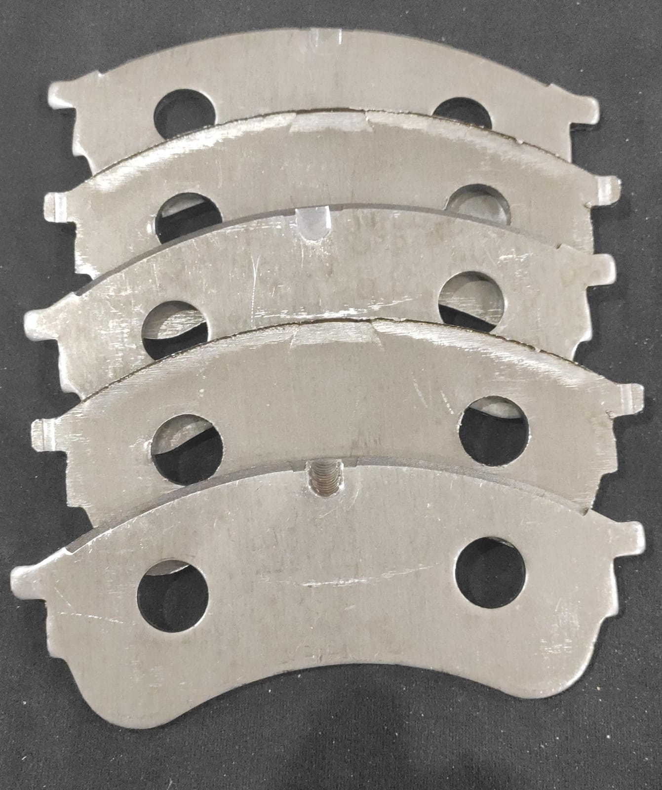 Lote de cinco peças metálicas usinadas em forma de arco, empilhadas verticalmente sobre uma superfície escura. As peças possuem acabamento superficial liso, furos passantes e aberturas retangulares precisas, demonstrando capacidade de fresagem de contornos